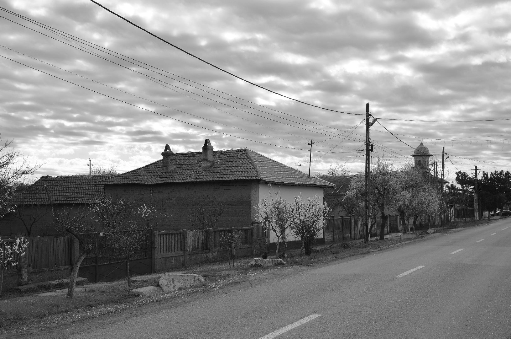 Vedere dintr-un sat din Câmpia Română, cu o locuință în prim-plan și silueta unei turle de biserică în plan secund.